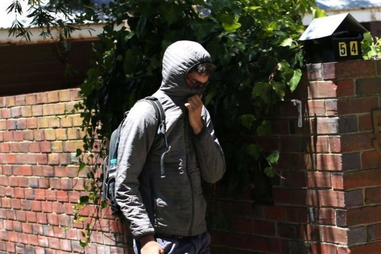 A man shields his face from cameras outside the home where nine backpackers overdosed.