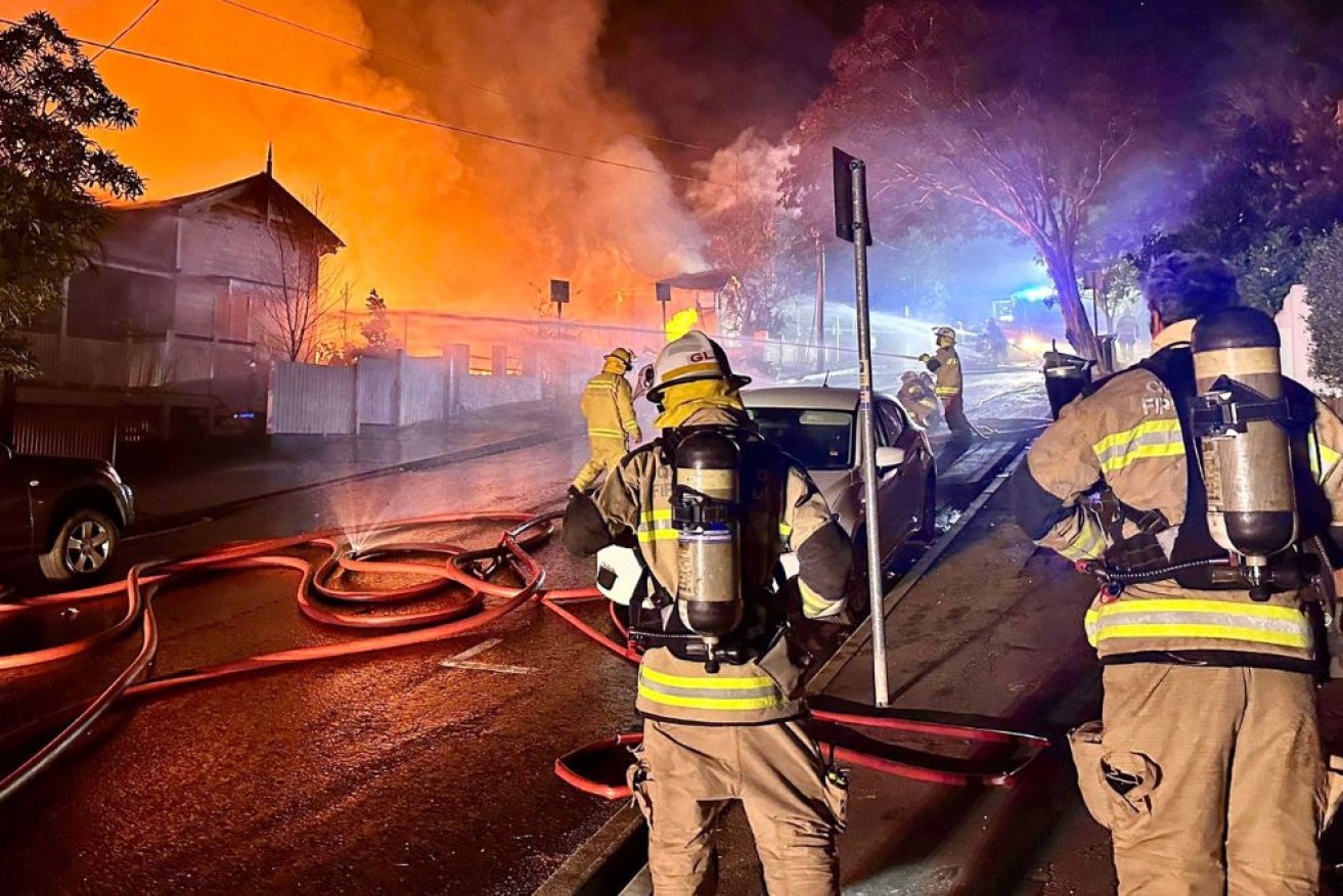 Firefighters try to contain flames chewing through four wooden houses in Brisbane. 