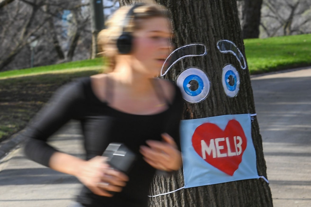 A woman jogs past a large face mask pinned to a tree in Melbourne on August 3, after the state announced new restrictions.