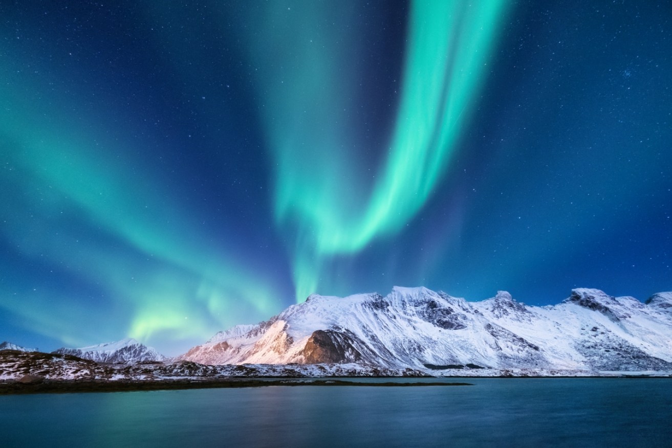 Aurora borealis on the Lofoten islands, Norway. Green northern lights above mountains. Night sky with polar lights. Night winter landscape with aurora and reflection on the water surface.