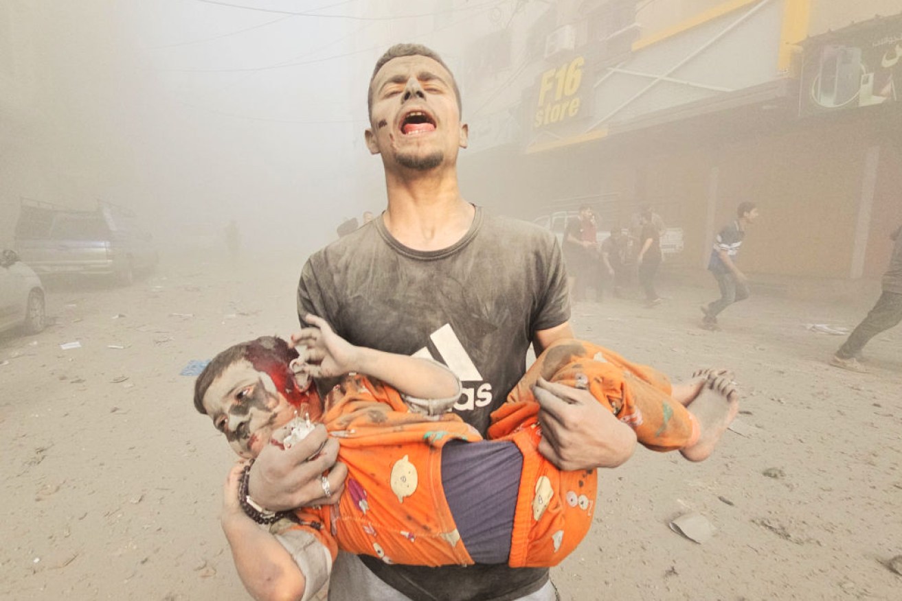 A Gaza resident carries a child from the rubble as the bombs continue to rain down.