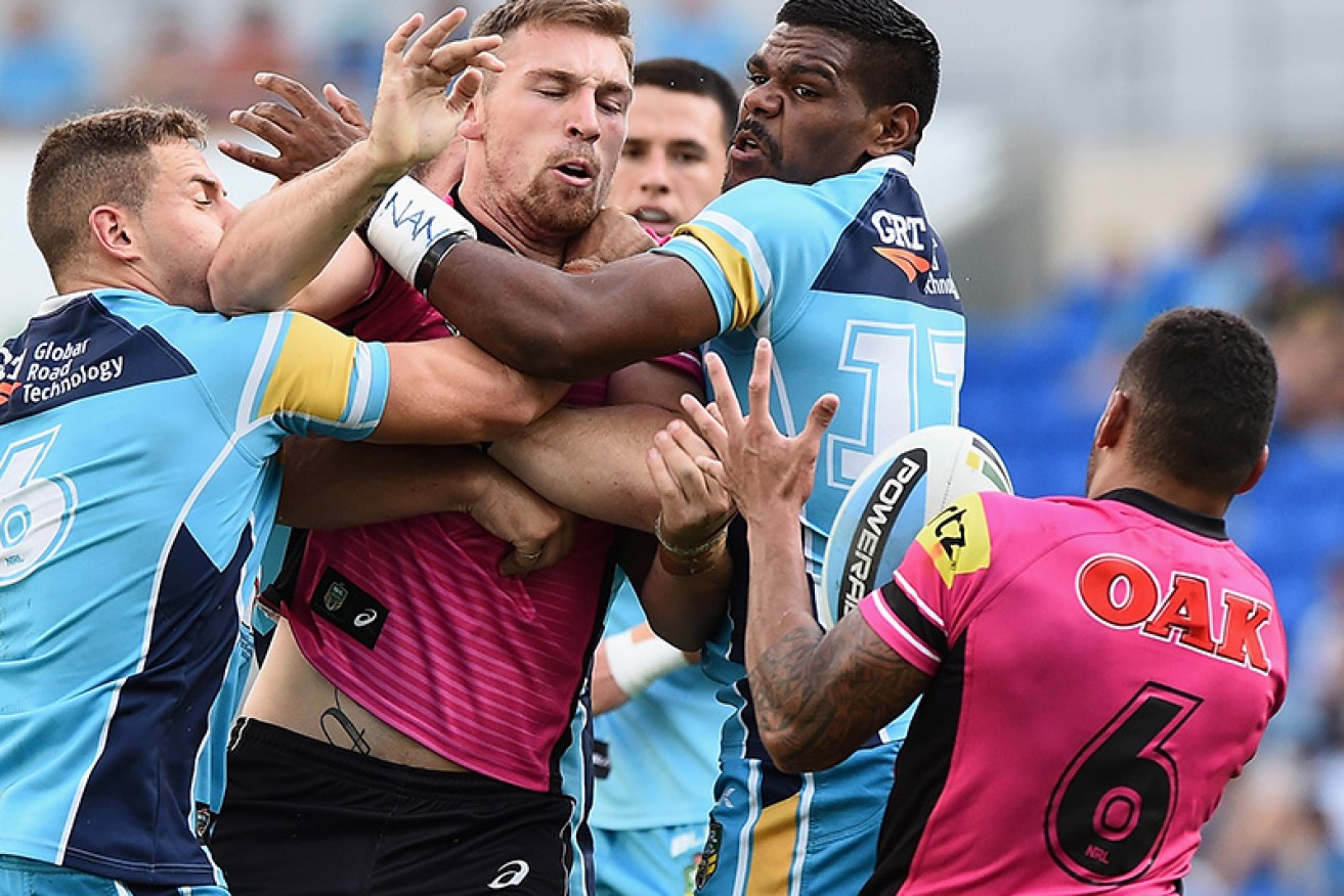 Gold Coast's Bryce Cartwright, centre, is being tackled over his anti-vaccination stand.