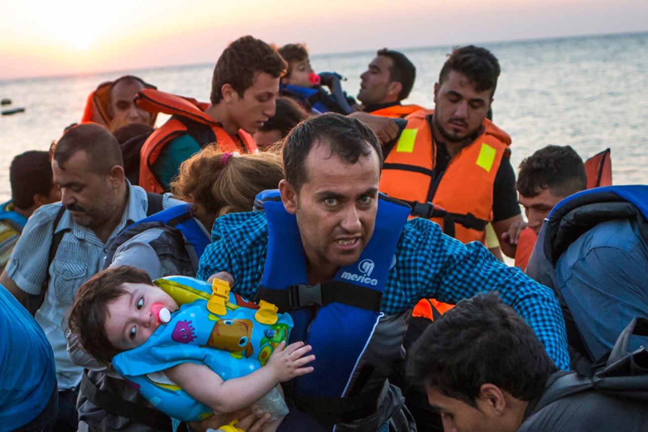 FILE - In this Aug. 13, 2015 file photo, a man carries a girl in his arm as they arrive with other migrants just after dawn on a dinghy after crossing from Turkey to the island of Kos in southeastern Greece. Greece has become the main gateway to Europe for tens of thousands of refugees and economic migrants, mainly Syrians fleeing war, as fighting in Libya has made the alternative route from north Africa to Italy increasingly dangerous. (AP Photo/Alexander Zemlianichenko, File)