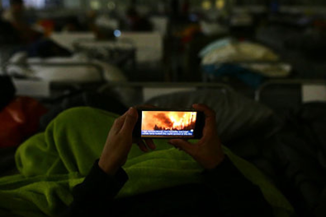 An evacuee looks at the fire on their mobile phone at a makeshift evacuee center in Lac la Biche. Photo: Getty