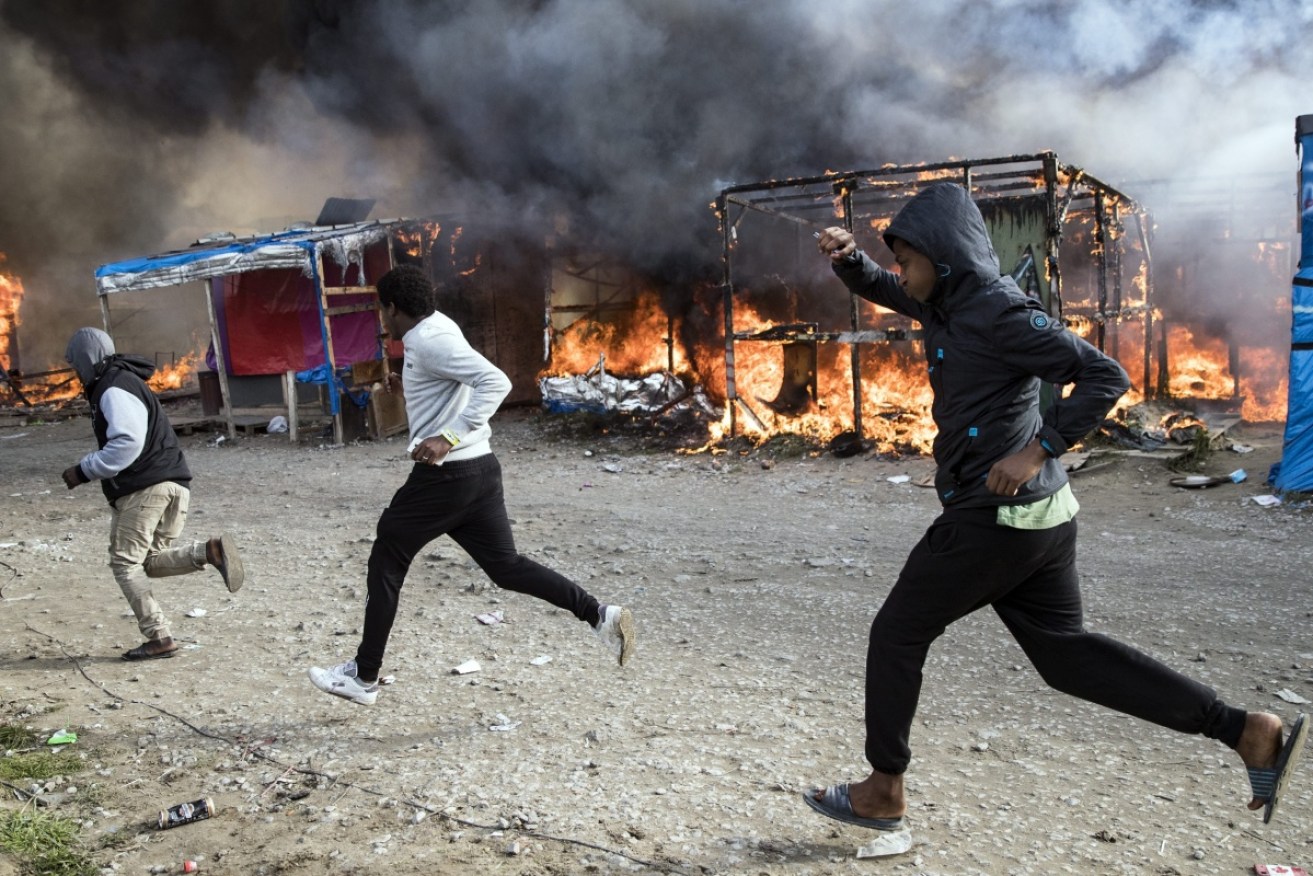 Migrants run past tents and shacks on fire during the evacuation of the 'Jungle' in Calais