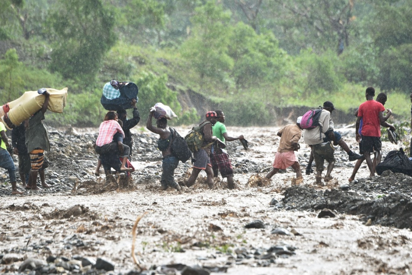 Haitians cross a river where a bridge collapsed during Hurricane Matthew, as they begin the grim and messy task of cleaning up.