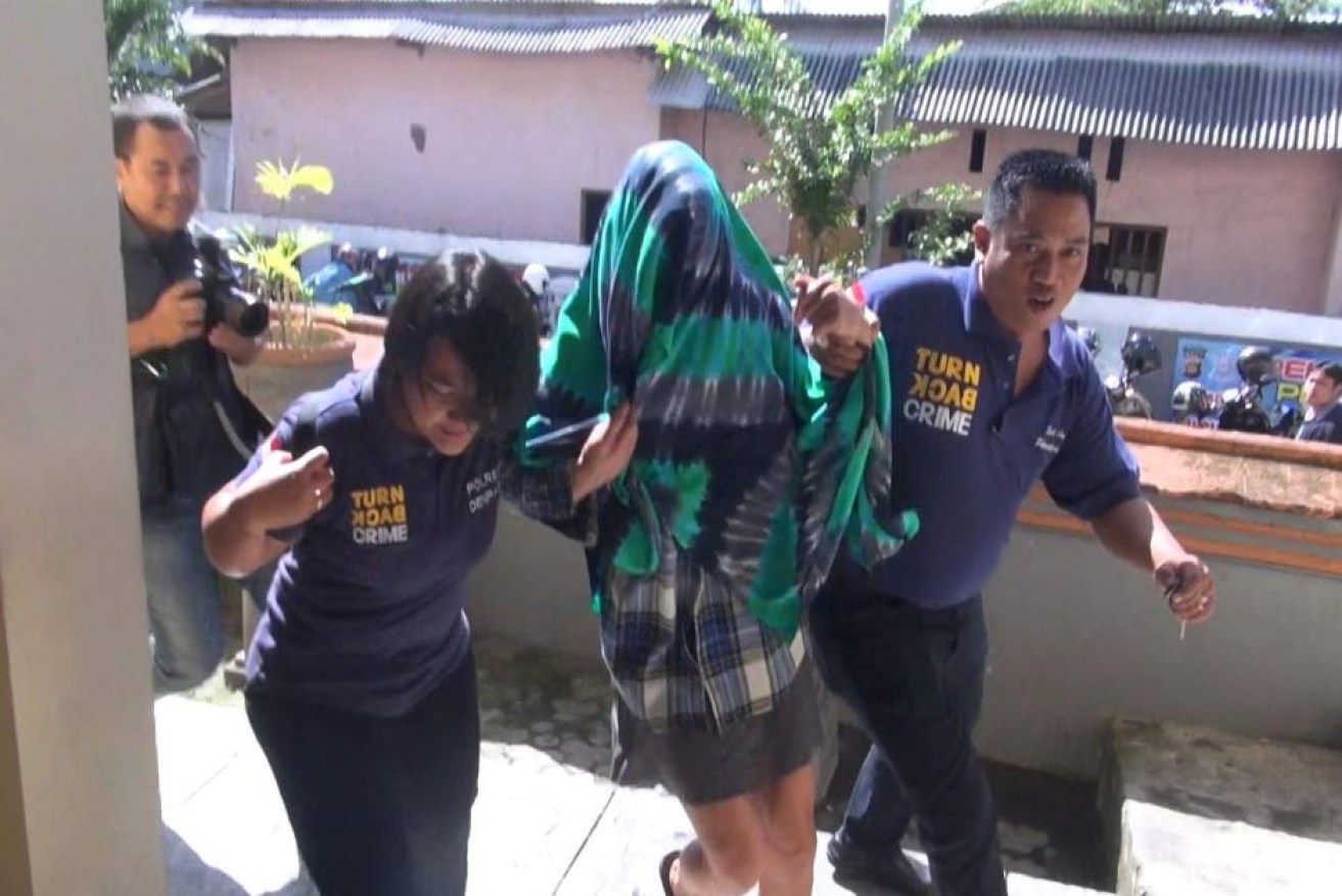 Sara Connor wears a sarong over her head as she is escorted to a Bali hospital.