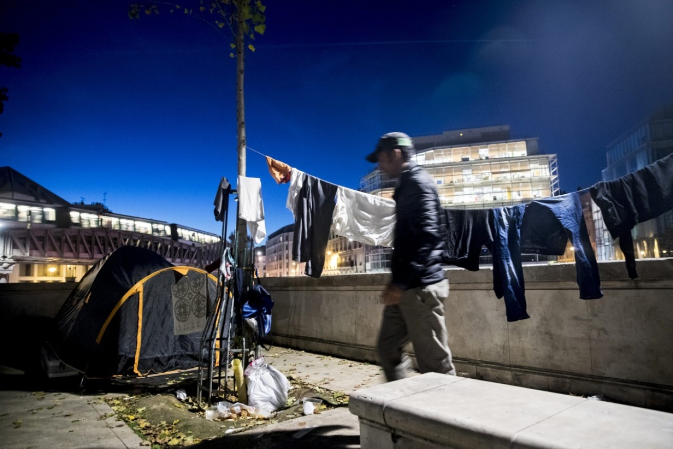 An Afghan migrant checks if his clothes have dried while a metro train passes his makeshift camp in the 19th district of Paris.