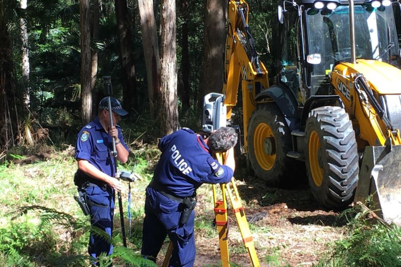 Police officers and a digger work at the search area.