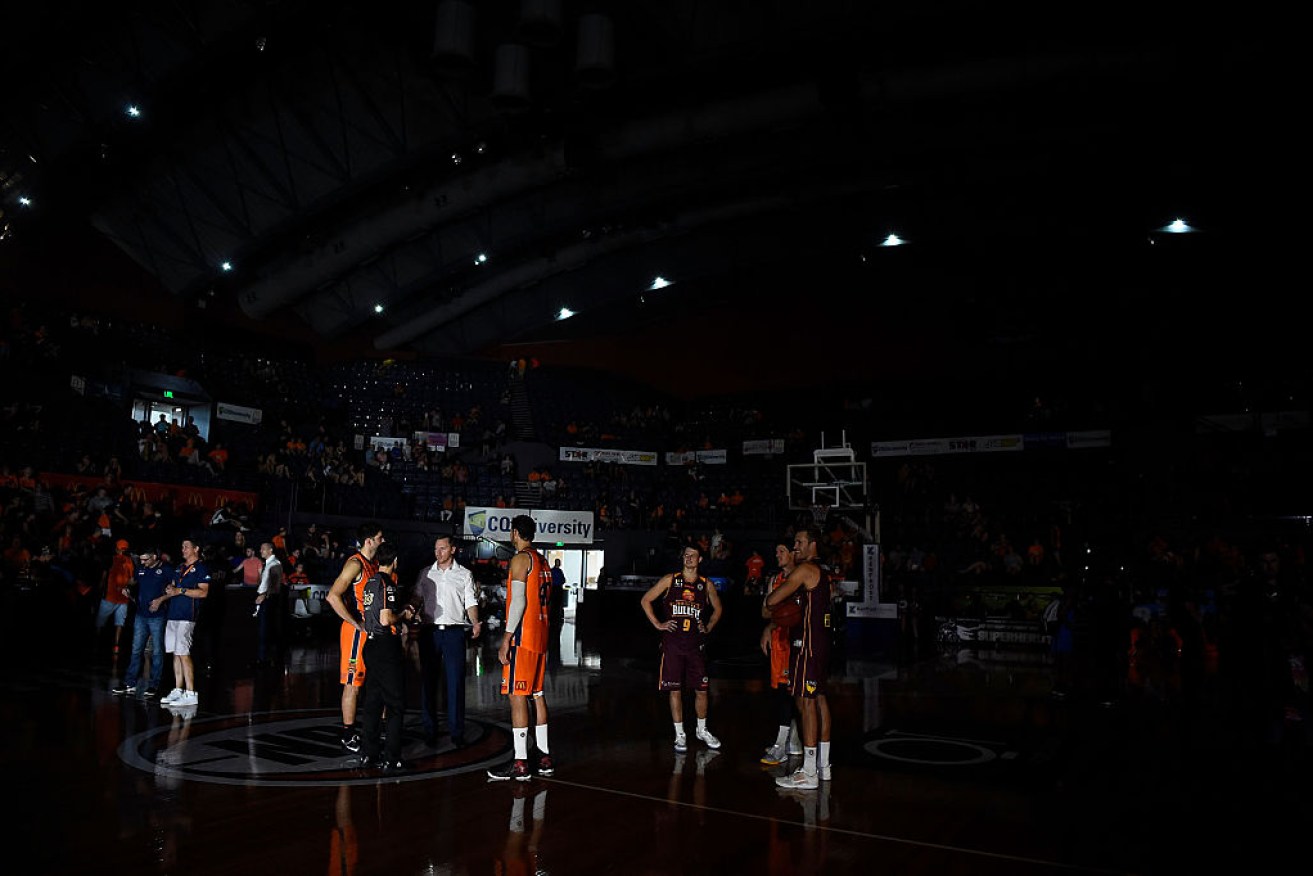 Taipans and Bullets players stand on court during a blackout in the final quarter of their clash.