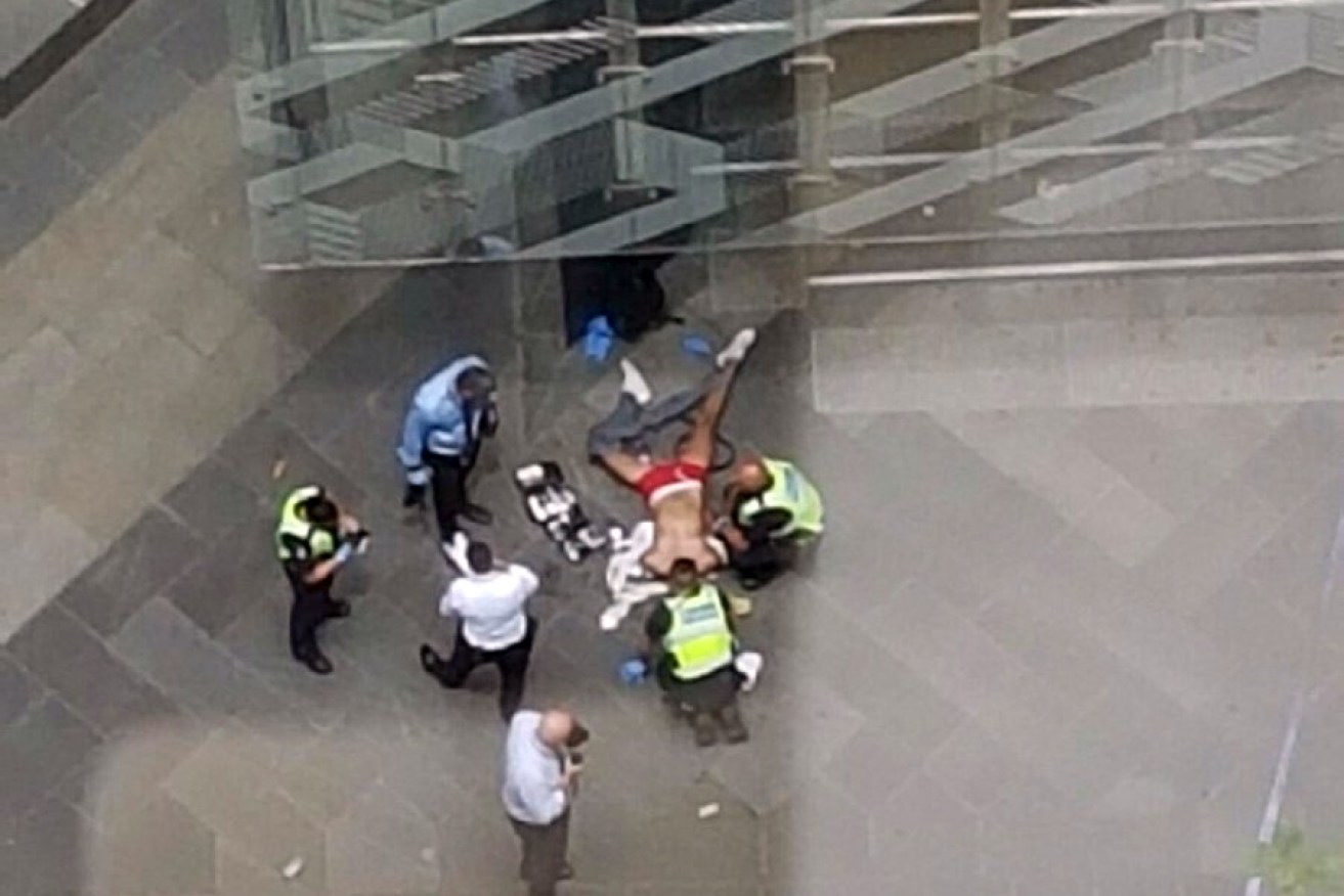 A man lies on the ground surrounded by police after the incident in Melbourne's CBD. 
