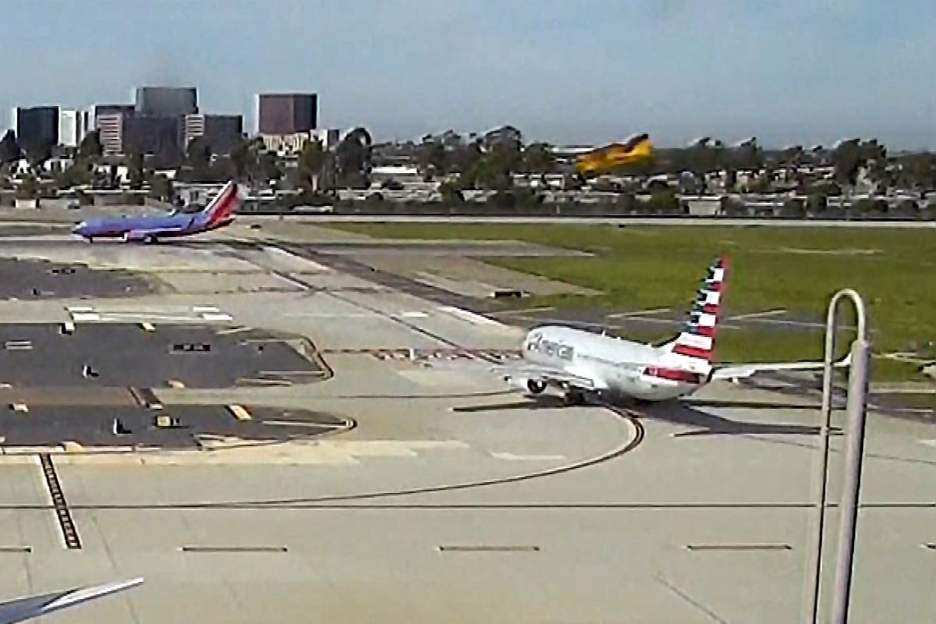 Harrison Ford's yellow plane comes in to land above a passenger jet.