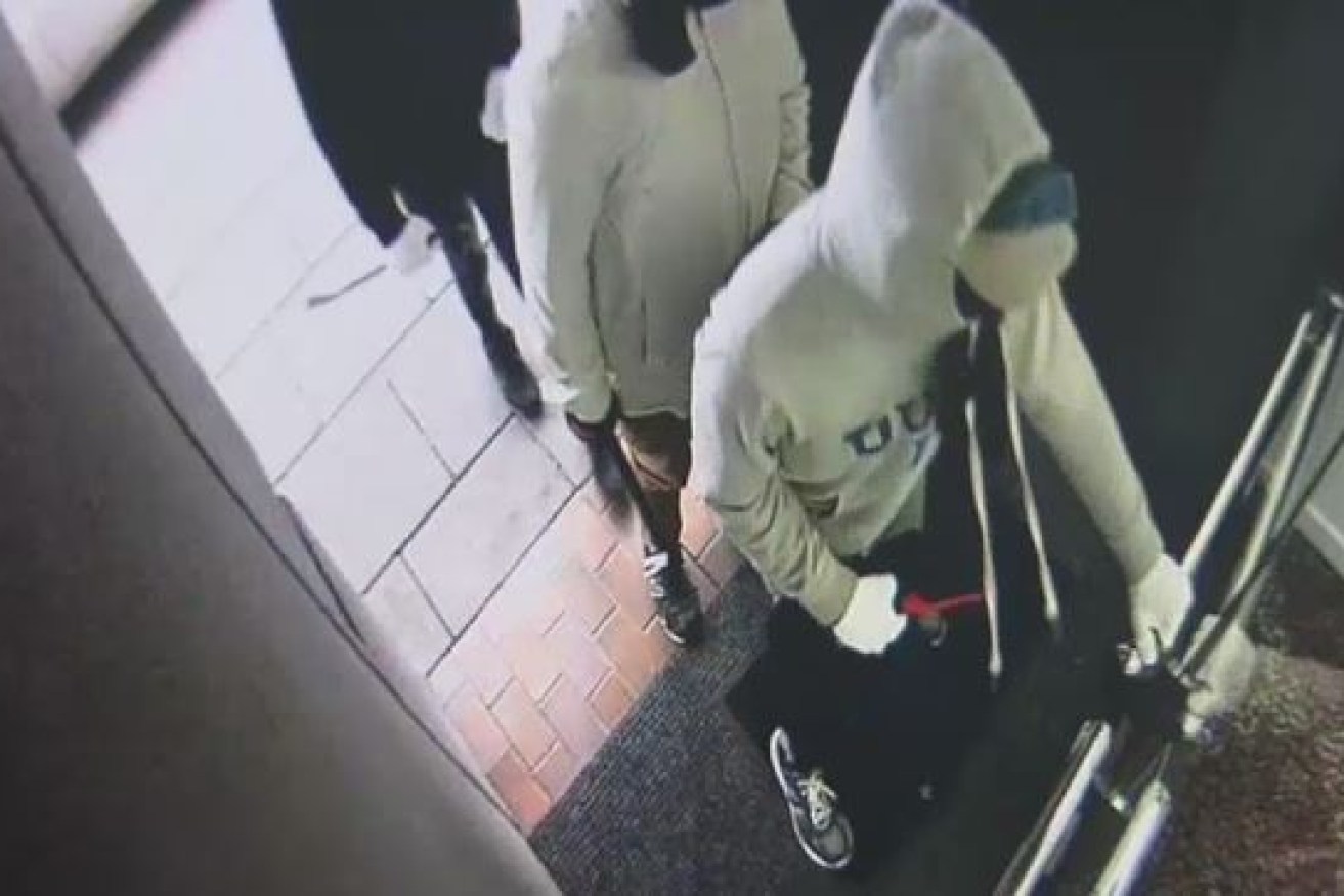 Hooded and masked, the four bandits attack the store's locked glass door with hammers to gain entry.