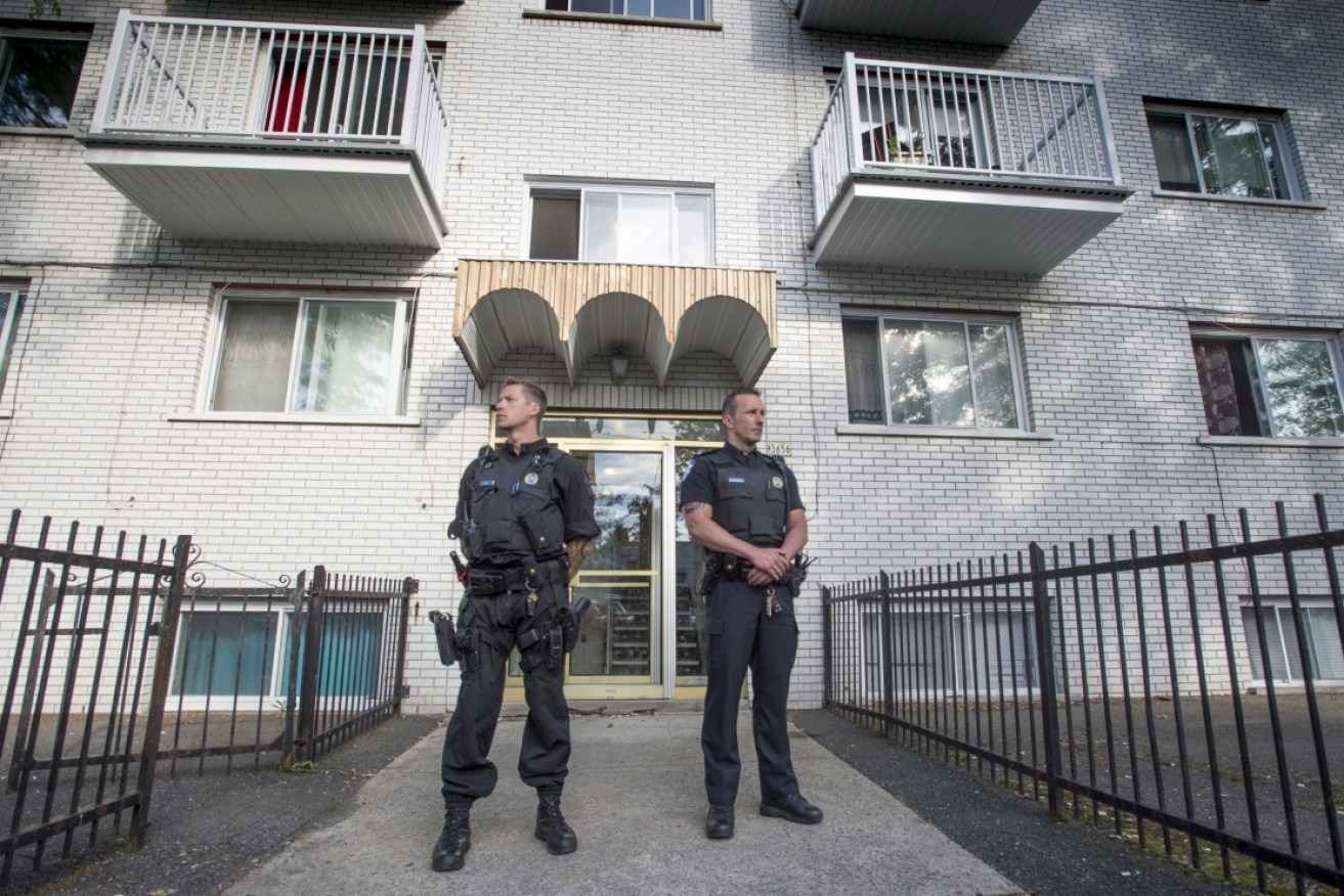Police stand guard outside apartment building in Montreal after the stabbing of a police officer at a Michigan airport.
