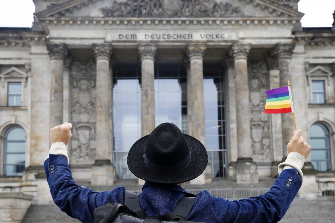 A man with a rainbow flag gestures towards the Reichstag building housing the German parliament.