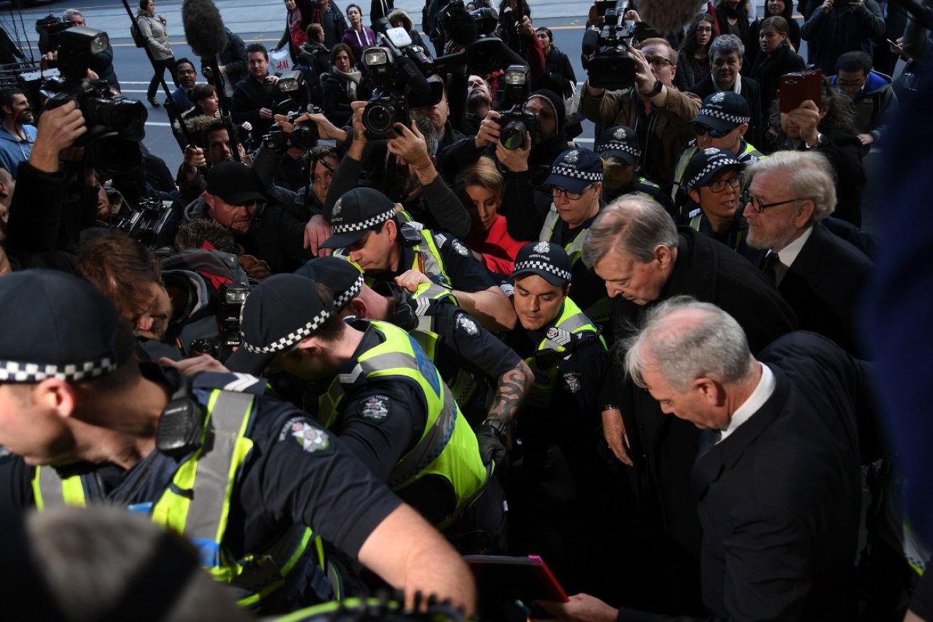 A scrum of media, police and protesters welcomed Cardinal Pell  to court in July, 2017.