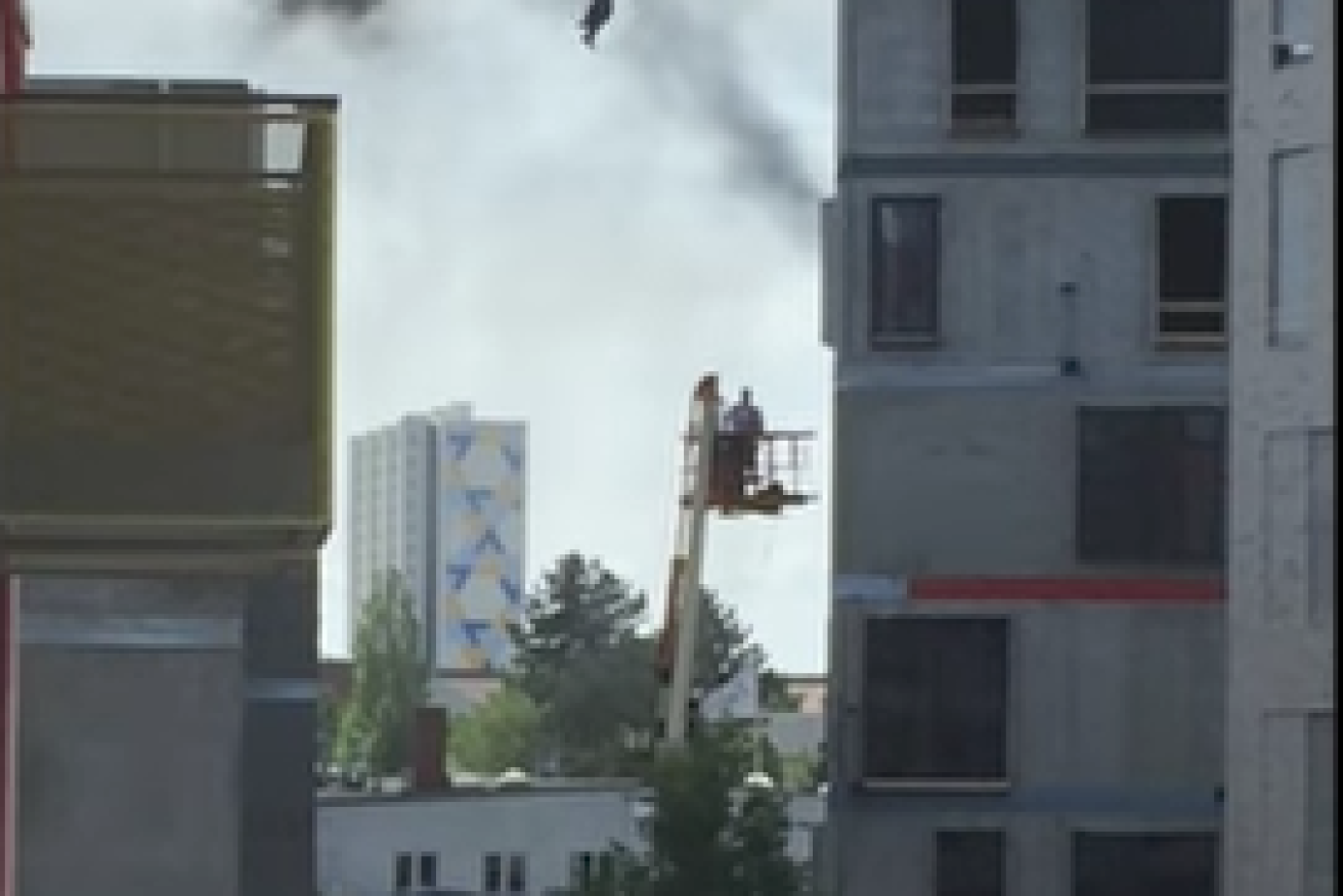 A roofer has been lowered to safety from a burning building by grabbing onto a crane hook