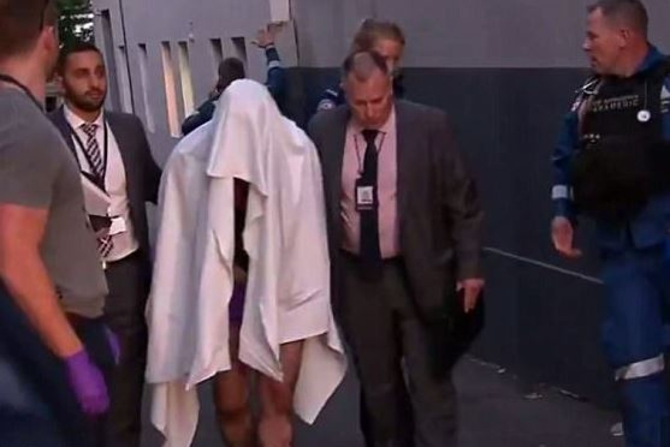 Covered by a sheet and said by witnesses to be bleeding, a man is led from the terrace house on Cleveland Street in Surry Hills.