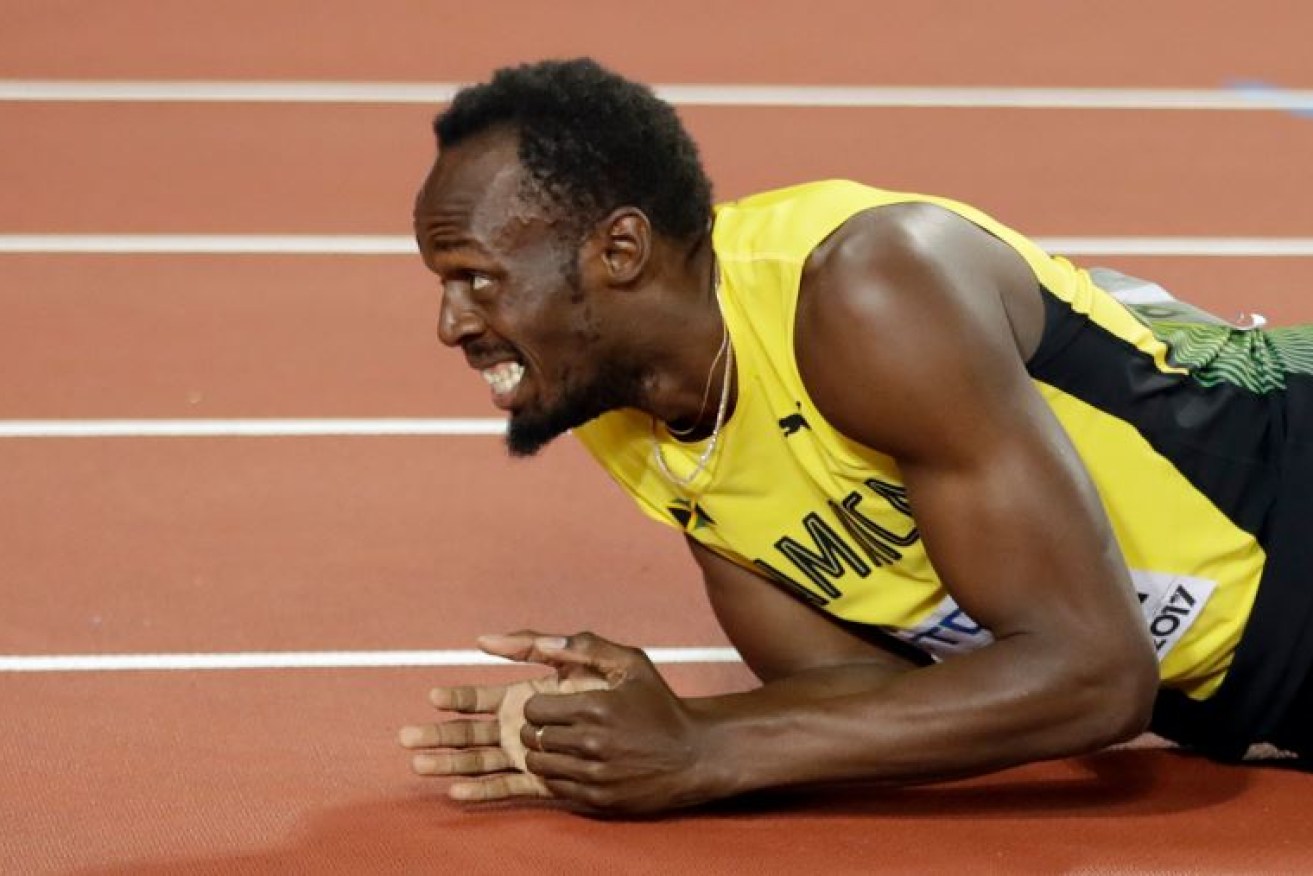 Usain Bolt grimaces in pain after hobbling across the finishing line, crippled by a ruptured hamstring in the home stretch.
