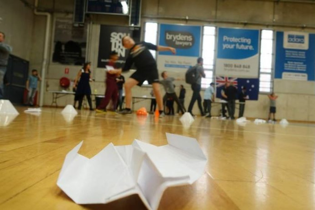 A paper-plane pilot launches his design on a floor littered with rivals' best efforts.