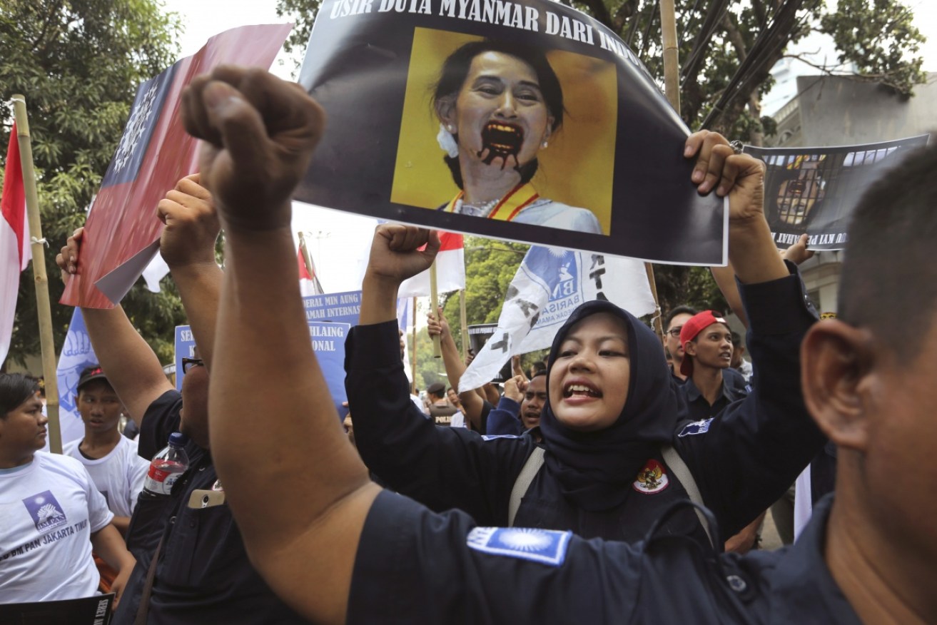 A Muslim woman protests in Myanmar holding a poster bearing a defaced portrait of Aung San Suu Kyi.
