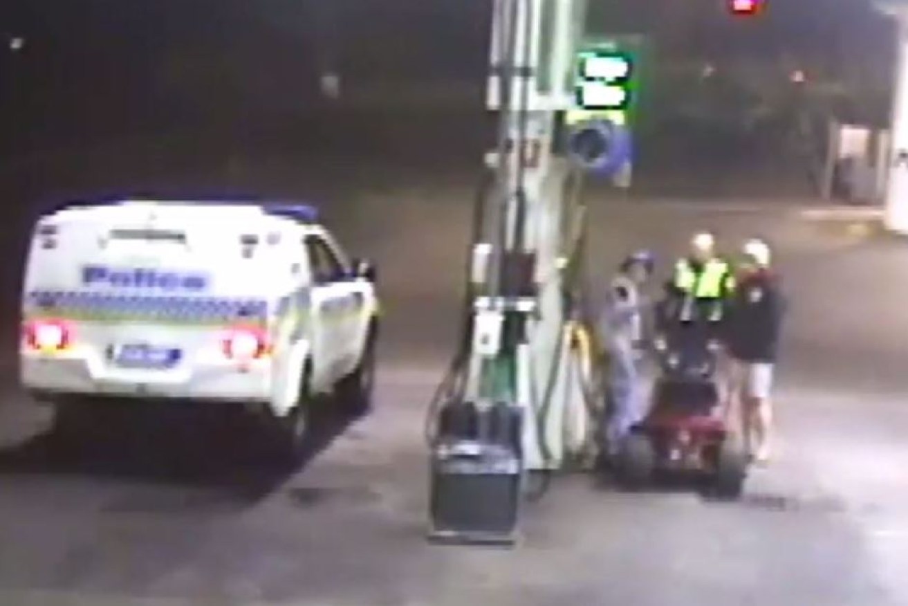 Police speak to a man who rode a lawnmower into a Tasmanian service station, as his companion watches on.