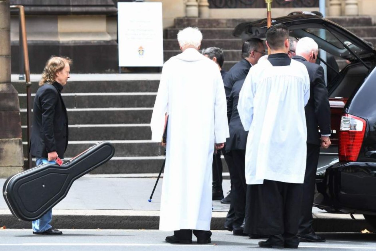 Angus Young carries a guitar to his brother's hearse after the service.