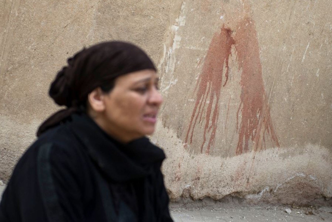 Dazedf and distraught, a sobbing woman  walks past bloodstains and bullet holes on the wall of the Cairo church. 