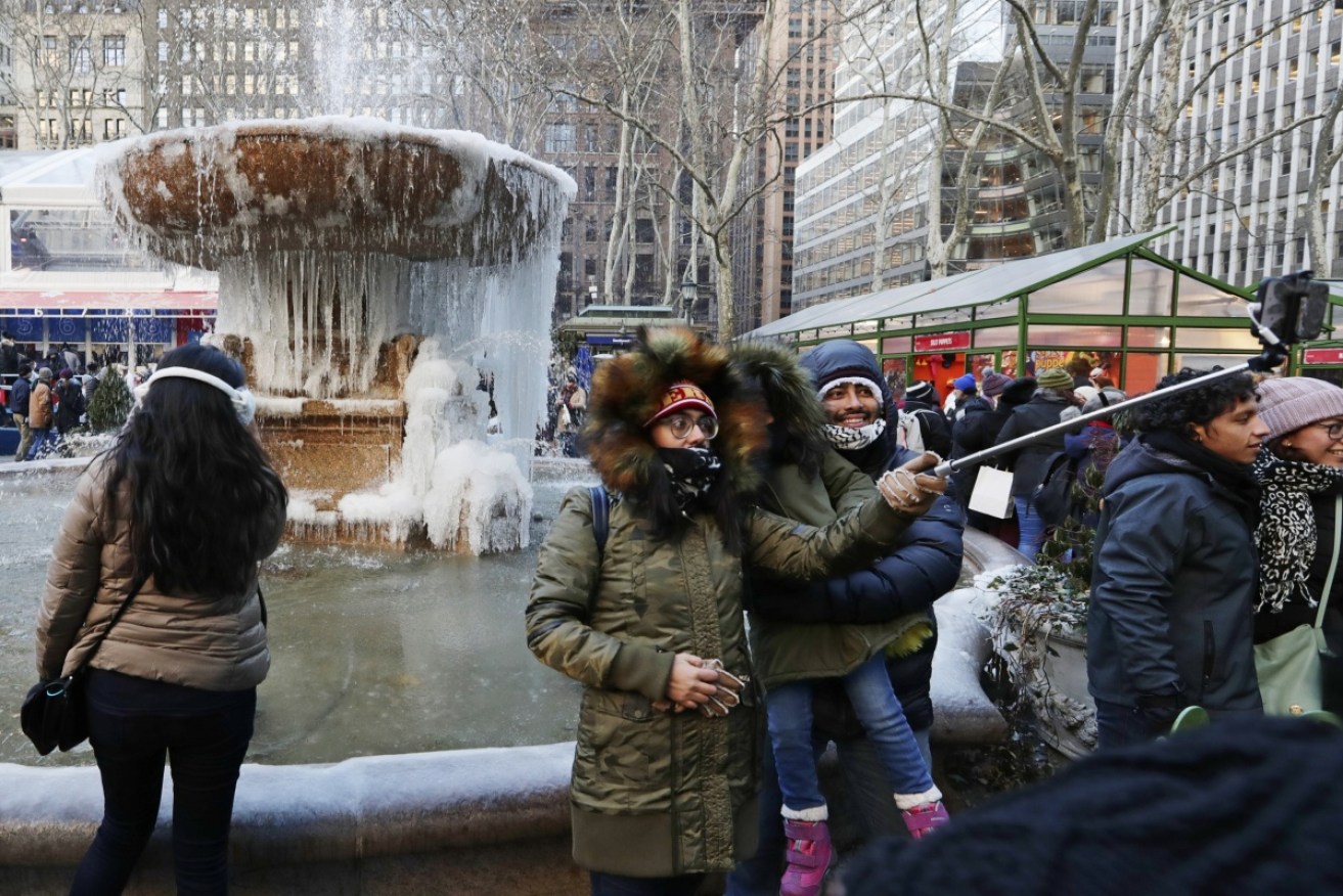 People take selfies in front of a frozen water fountain at Bryant Park on December 28, 2017, in New York.