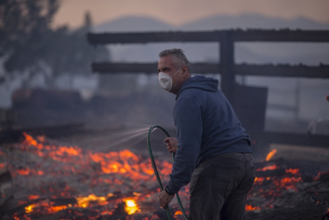 A resident holds a leaking hose on his burning property in Sunland, California.