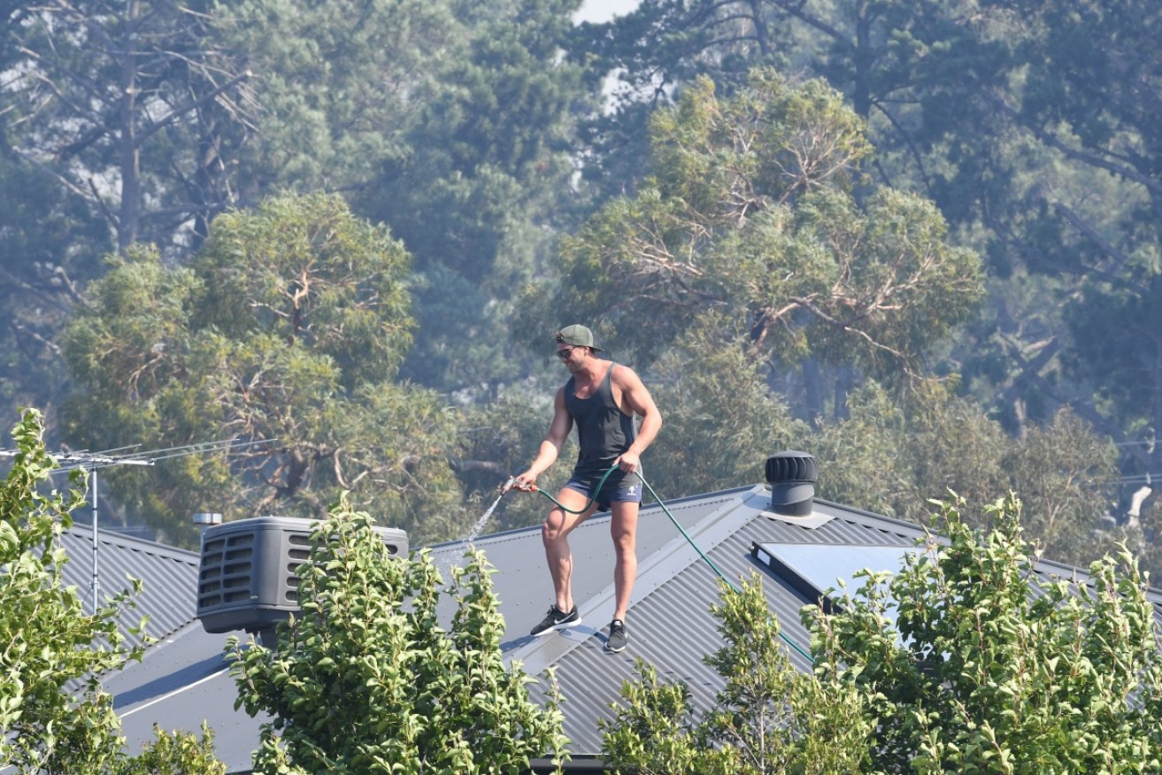 A man hoses down his roof in Carrum Downs, Victoria, where an out-of-control fire raged on Saturday afternoon.
