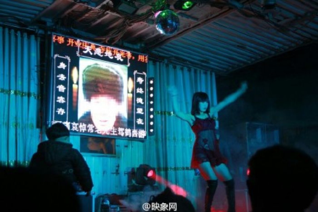 The face of the deceased is projected behind a funeral performer. 
