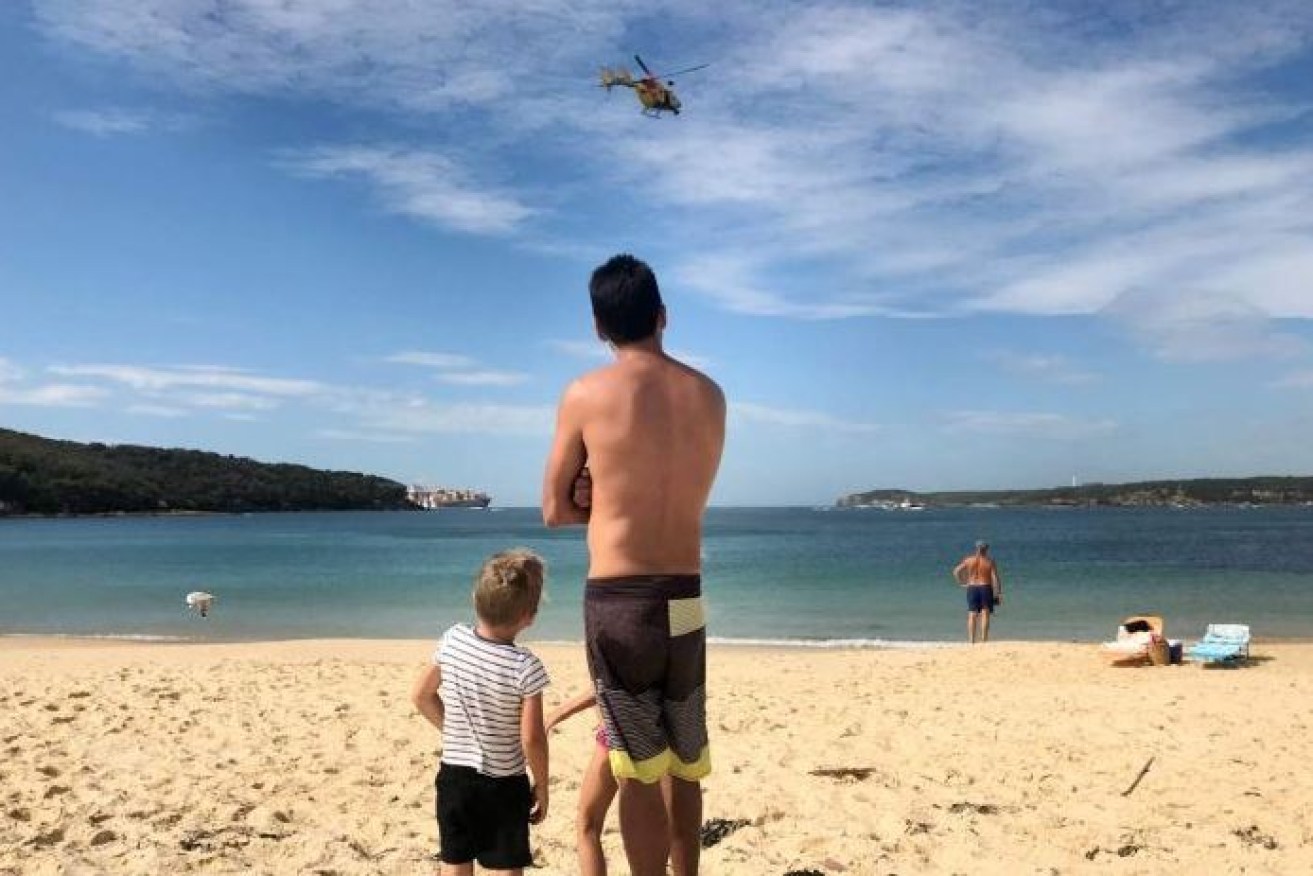 Banned from the water after the shark attack, would-be swimmers watch a chopper search for the marine predator.