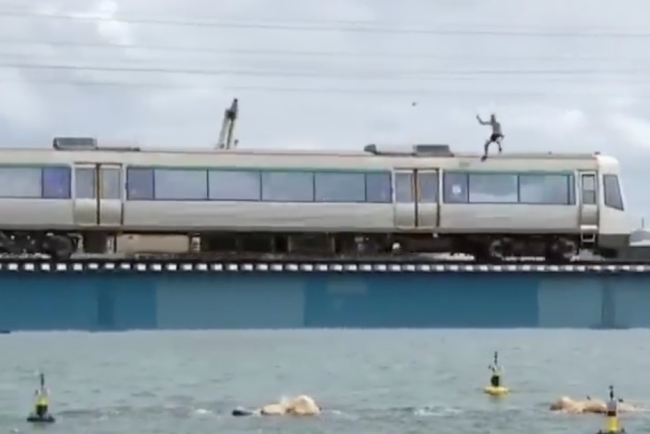 A screenshot of a man jumping from a train into the Swan River. 