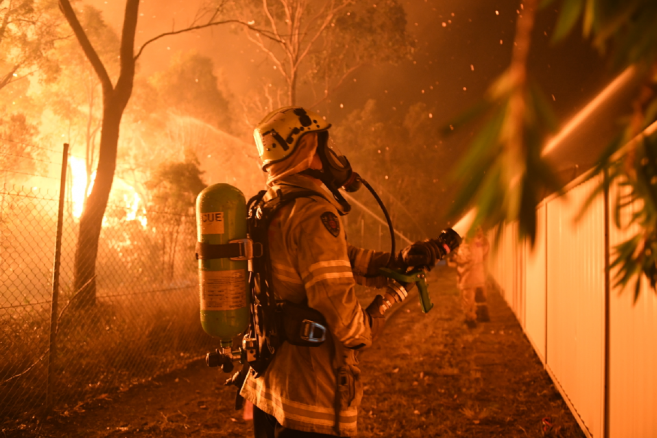 A firefighter hoses down an endangered home in south-west Sydney over the weekend.
