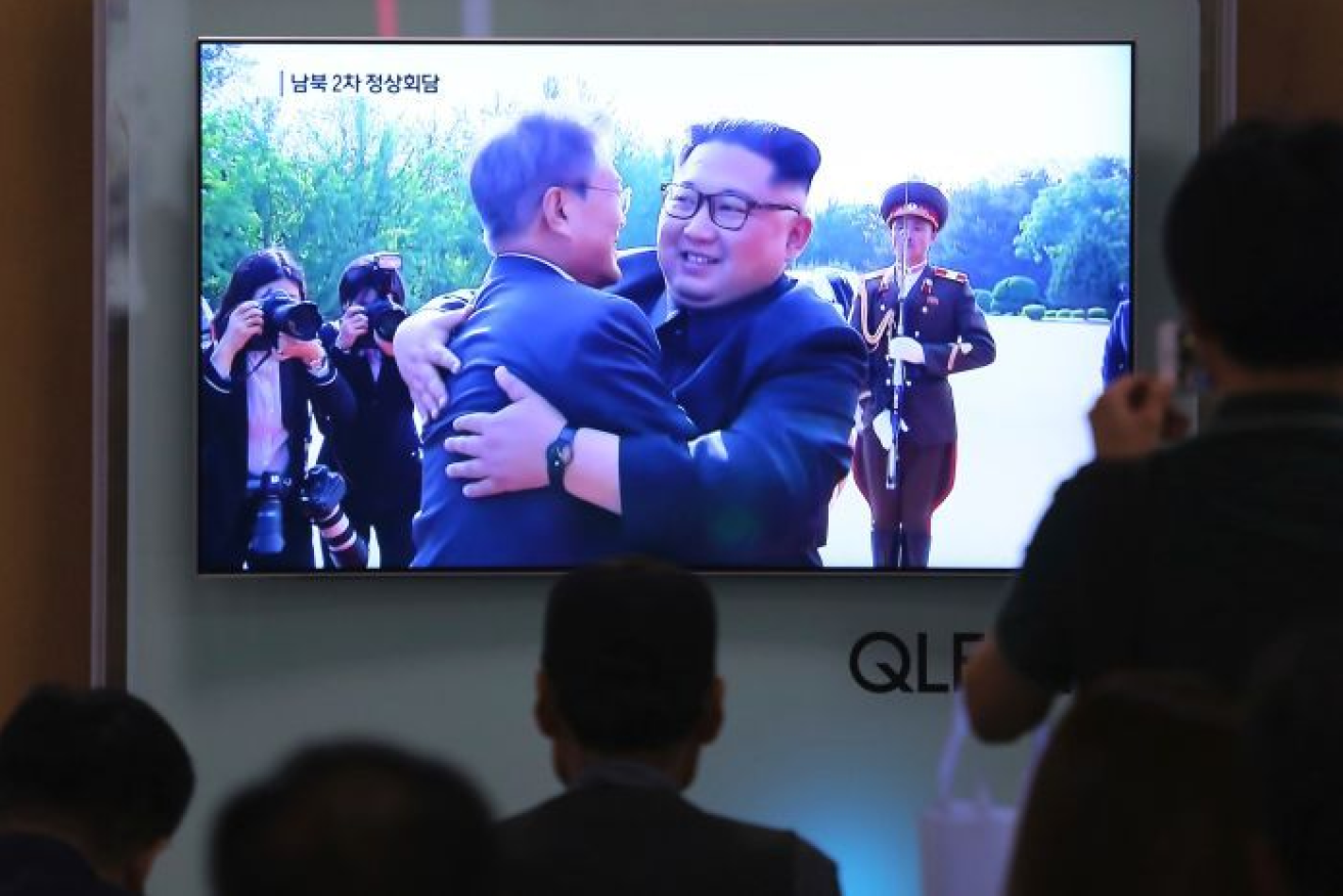 Kim Jong-un  and South Korea's Moon Jae In exchange hugs as Seoul commuters watch a train station TV.