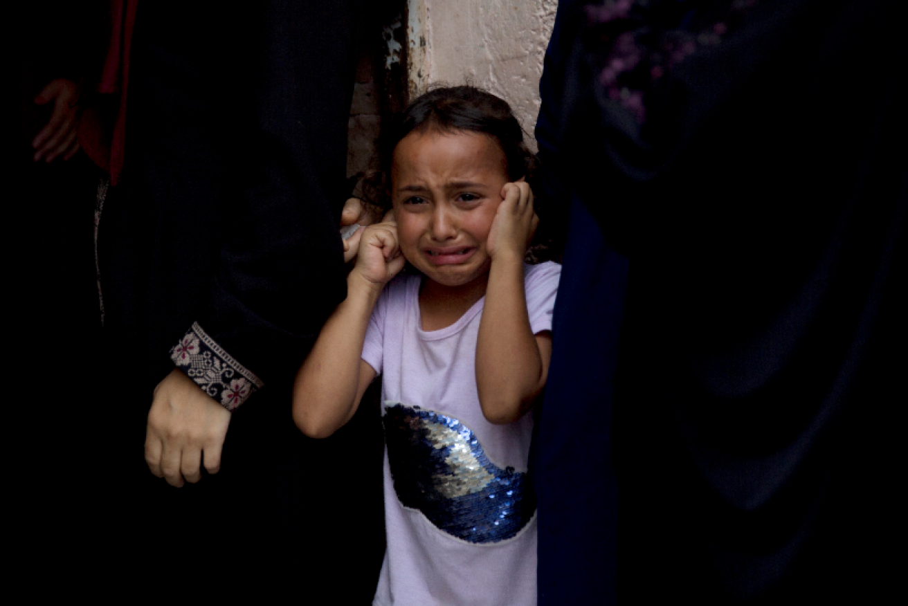 A sobbing girl blocks  the sound of a relative's funeral as the bombs rain down on Gaza.