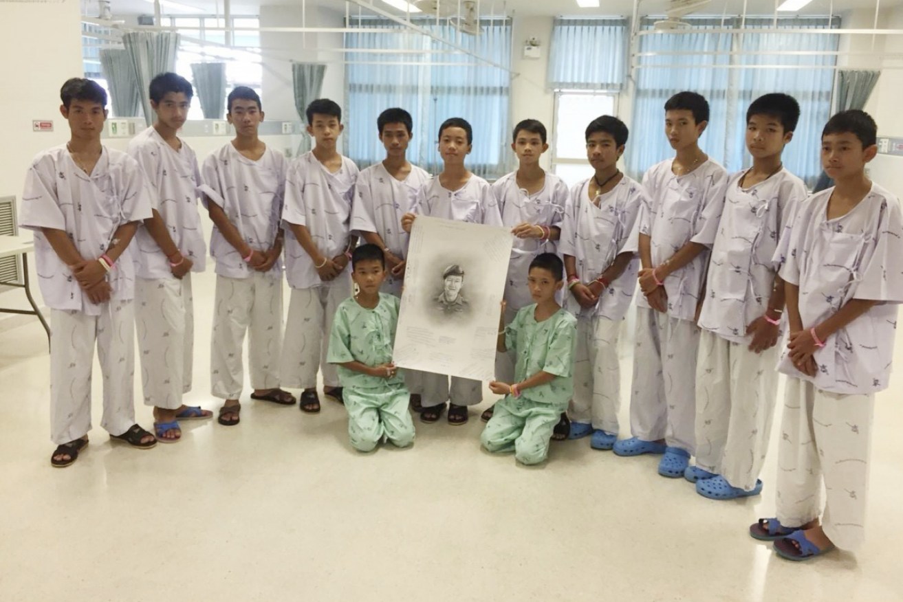 The Wild Boars pose with a sketch of the Thai Navy SEAL diver who died during their rescue.