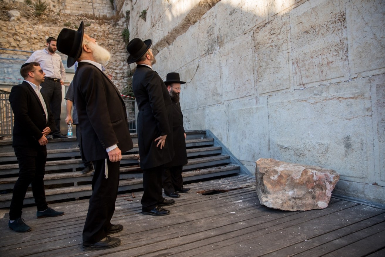 Rabbis inspect the wall, with the 100-kilogram stone at their feet.