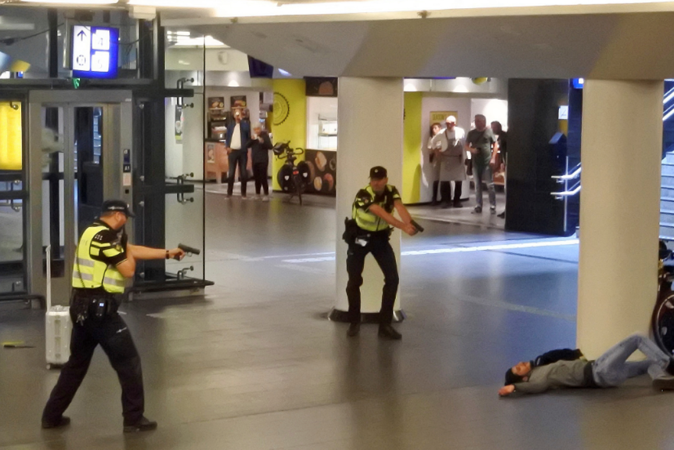 Dutch police keep their guns trained on the wounded suspect, who was shot after stabbing two US tourists in Amsterdam's main station.