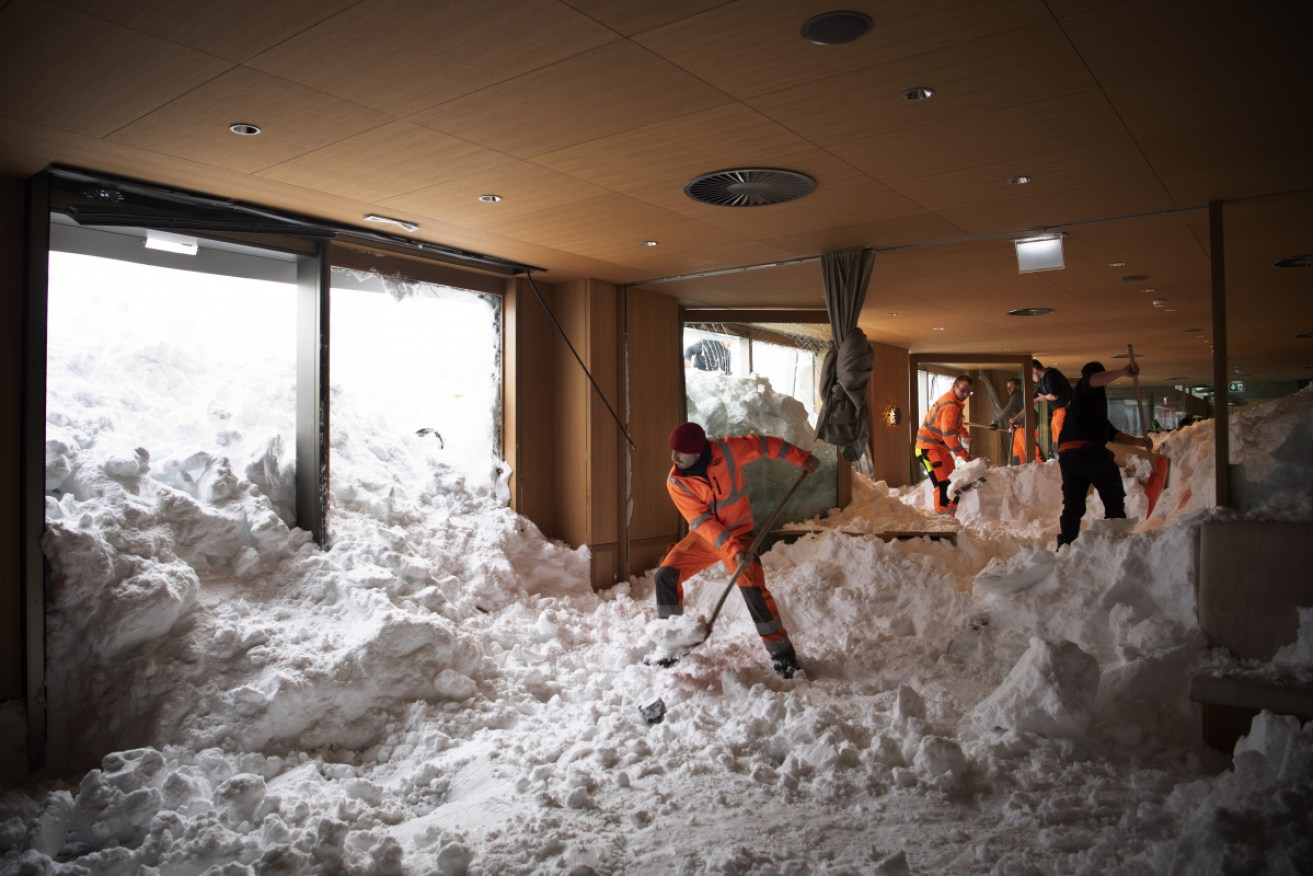People clear snow from inside the Hotel Saentis in Schwaegalp, Switzerland, on Friday Jan. 11, 2019, after an avalanche.