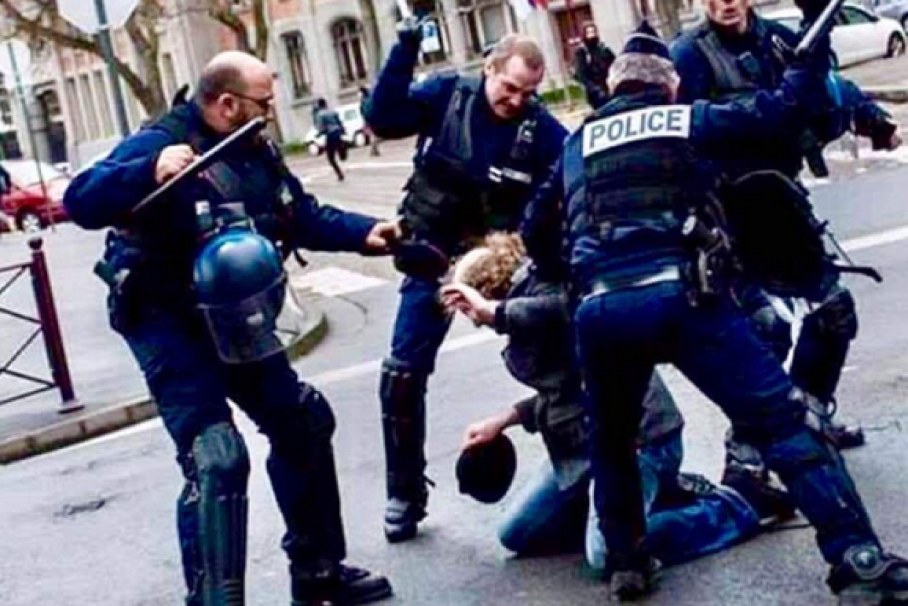 Riot police beat a protester as the streets of Paris once reek with the stench of smoke and tear gas.