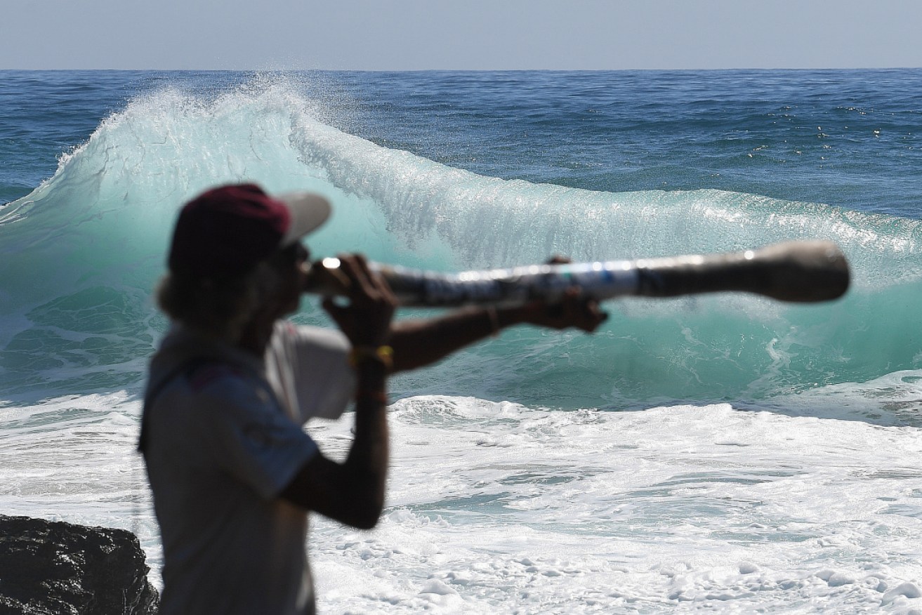 Didgeridoo player Russell Corowa is dwarfed by waves at Snapper Rocks on the Gold Coast on Tuesday.