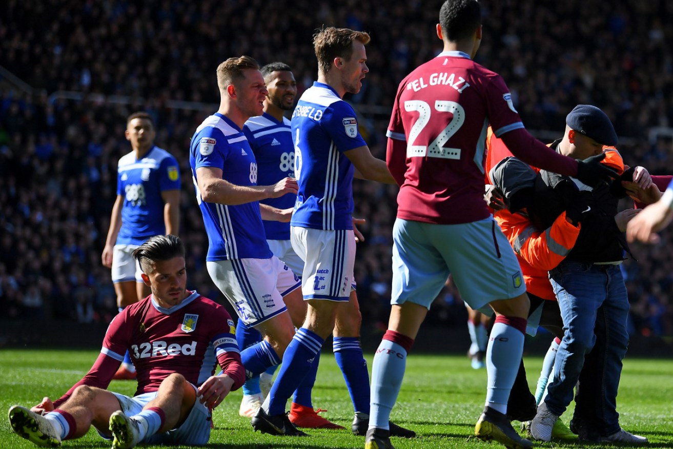 Jack Grealish sits on the ground as players and officials grapple with his attacker.  
