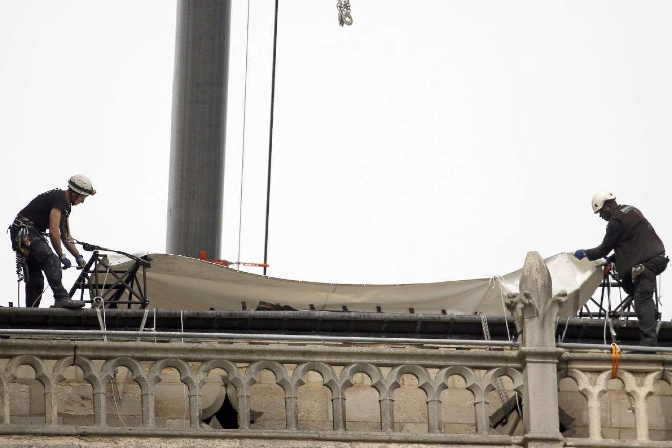 Workers drag tarpaulins across the fire-damaged roof of Notre Dame.