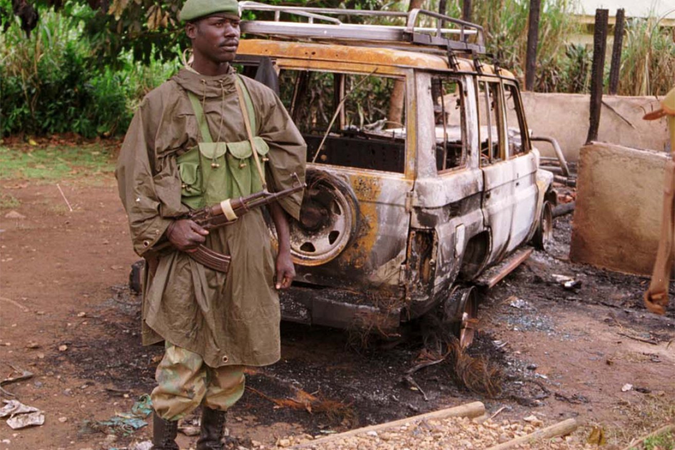 An Ugandan soldier stands by a burned car at the Bwindi National Park, where eight tourists were killed by Hutu militia in 1999.