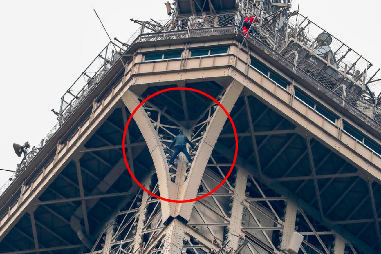 A man dressed in black held himself between two beams just under the top observation deck of the Eiffel Tower.