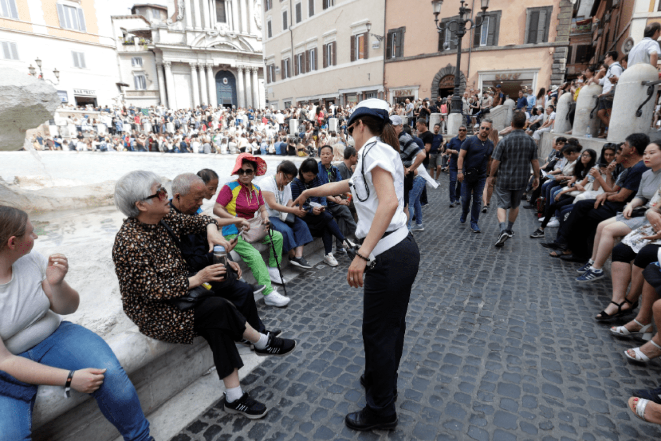 A bylaws officer lays down the law to a tourist caught eating on the wall of the famous Trevi Fountain.