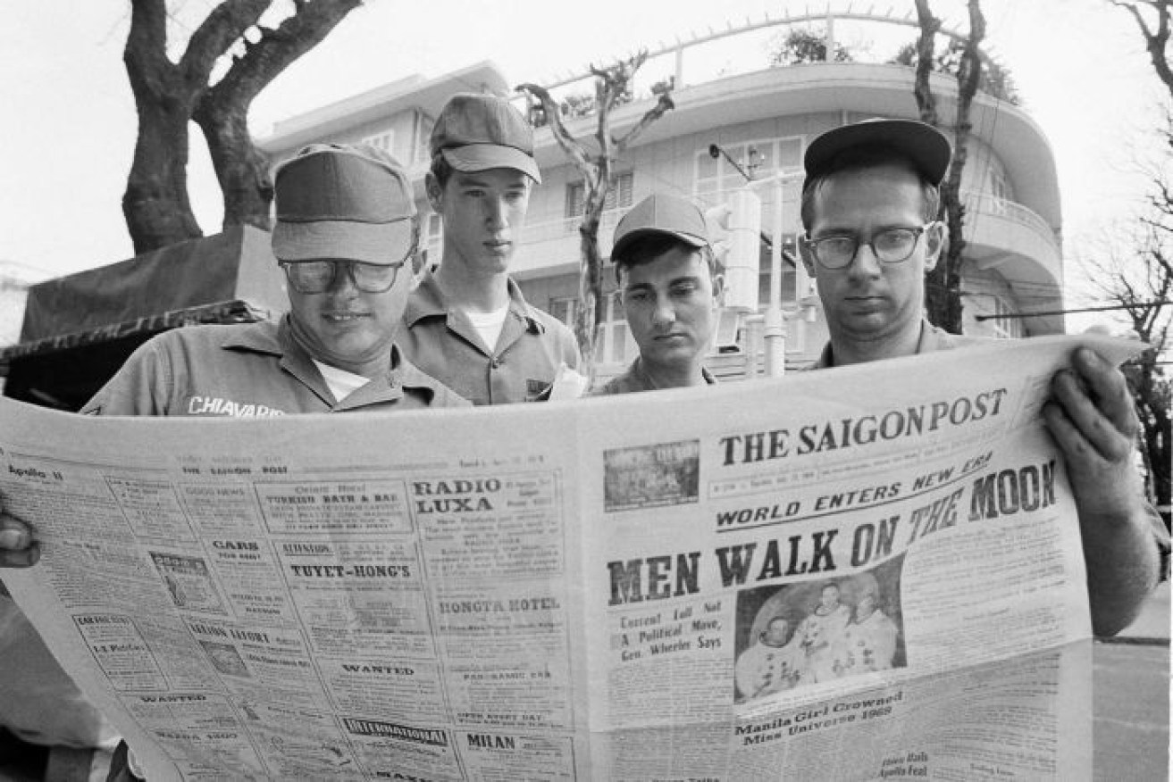 American servicemen in Vietnam read a newspaper headlining the Apollo 11 Moon landing. 