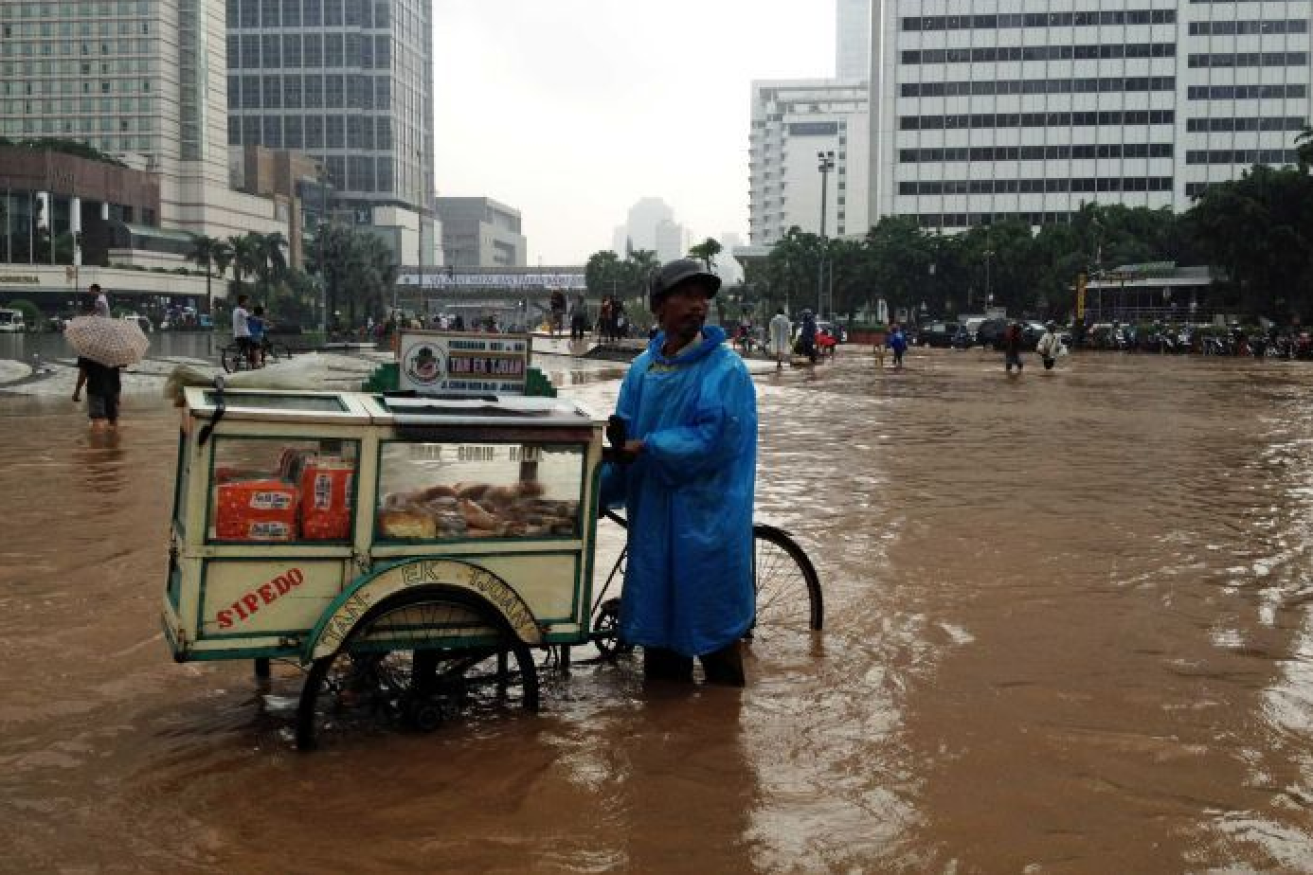 A street vendor wades kn-ee-deep through one of the inundations that regularly engulf Jakarta